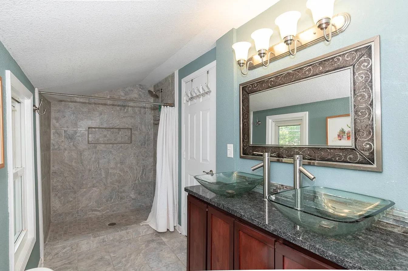 Bathroom — teal walls with dual glass vessel sinks and walk-in tile shower