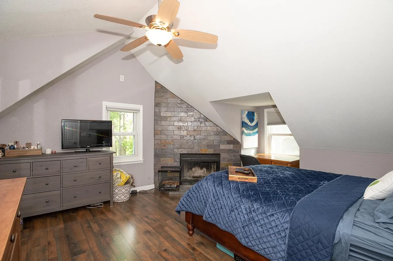 Bedroom — attic master suite with stone fireplace, navy quilt and dark hardwood floors