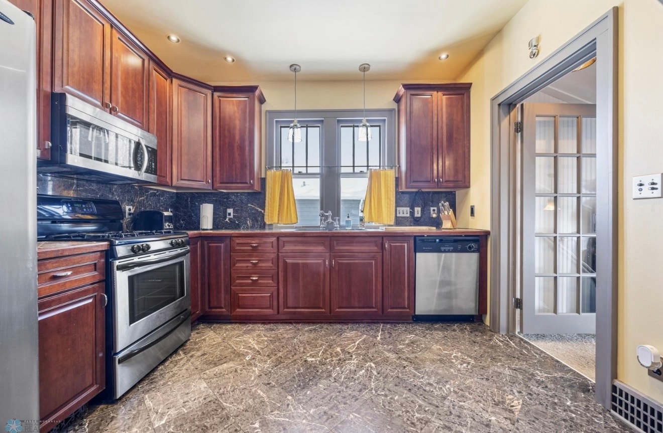 Kitchen — cherry cabinets with stainless appliances, yellow curtains and marble backsplash